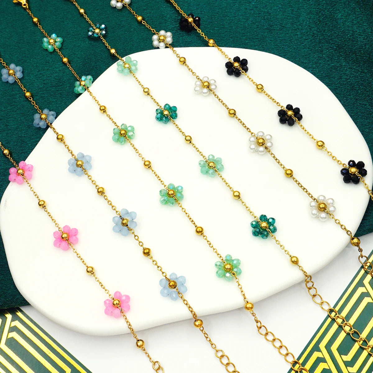 A collection of pastel flower beaded boho bracelets on a white ceramic display with green velvet background.
